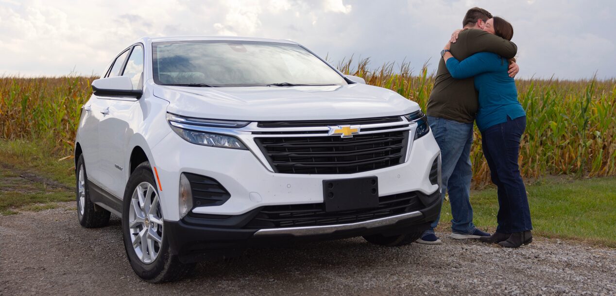 A mother and son hugging while standing next to their Chevy vehicle.