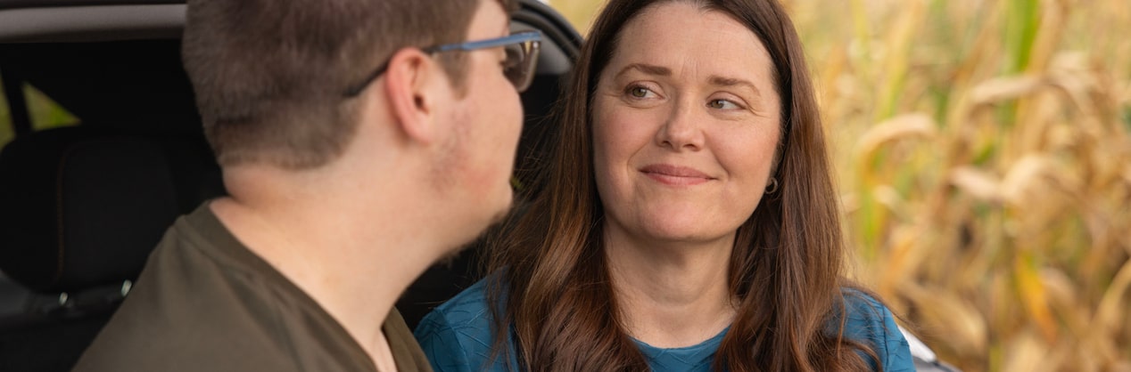 A mother and son sitting in the back of their vehicle, looking at each other.