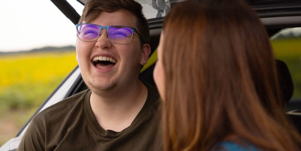 A son laughing while sitting in the back of the vehicle with the trunk open.