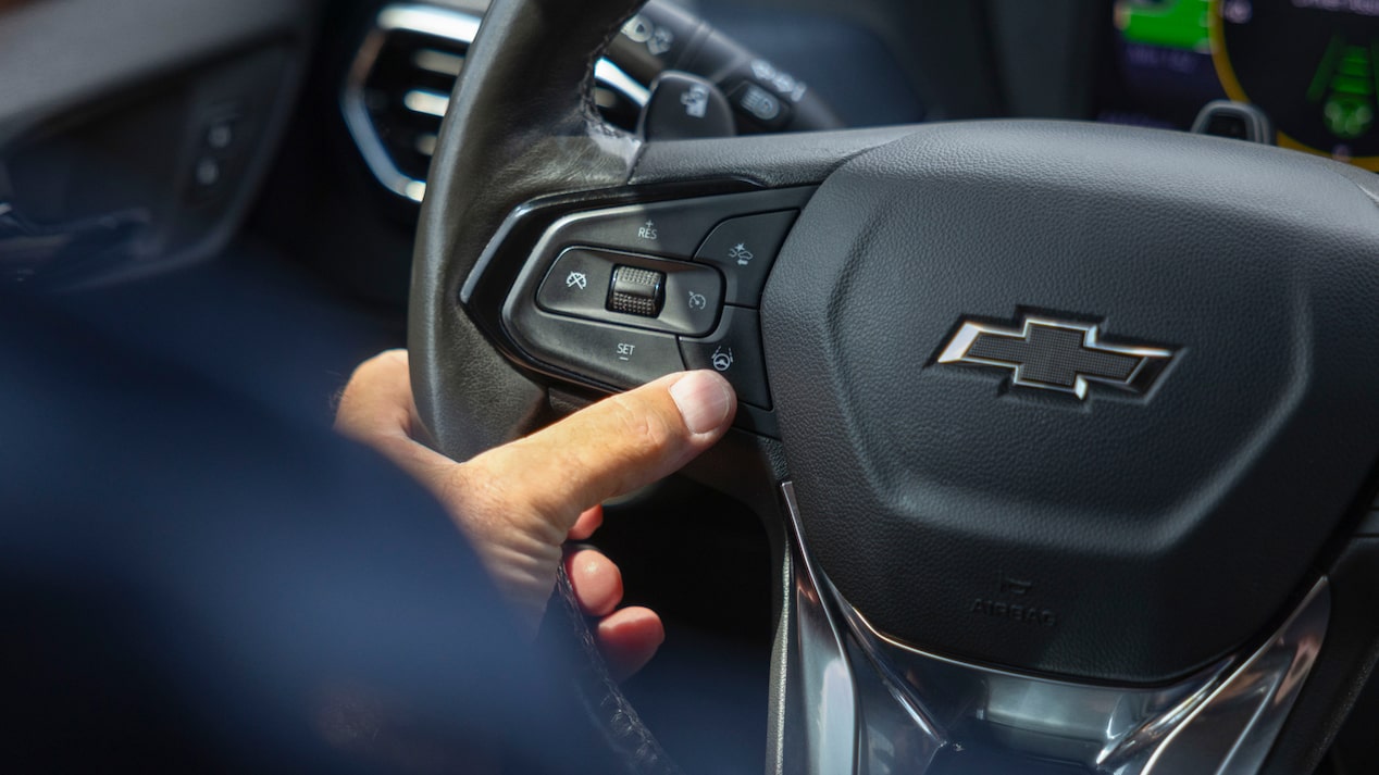 A hand presses a button on the steering wheel of a Chevrolet Bolt EUV, engaging a Super Cruise feature.