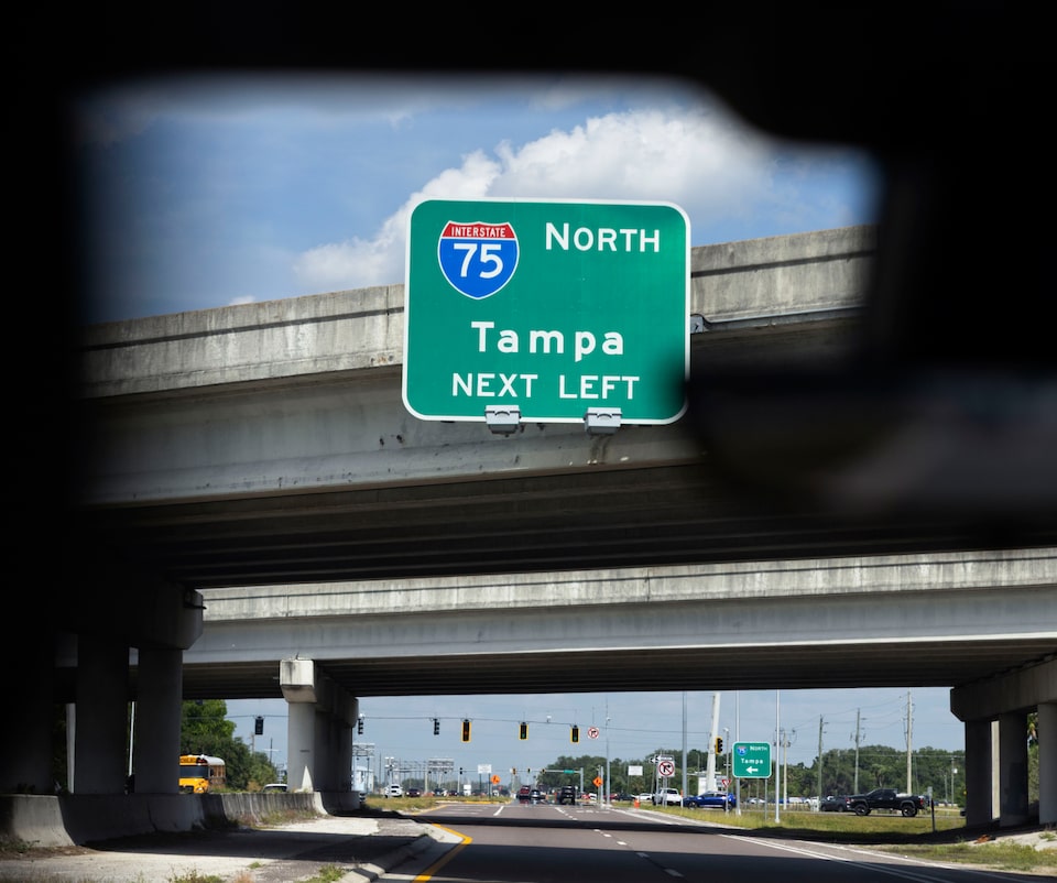 A view through a car windshield shows a green Interstate 75 North Tampa sign over a highway underpass.