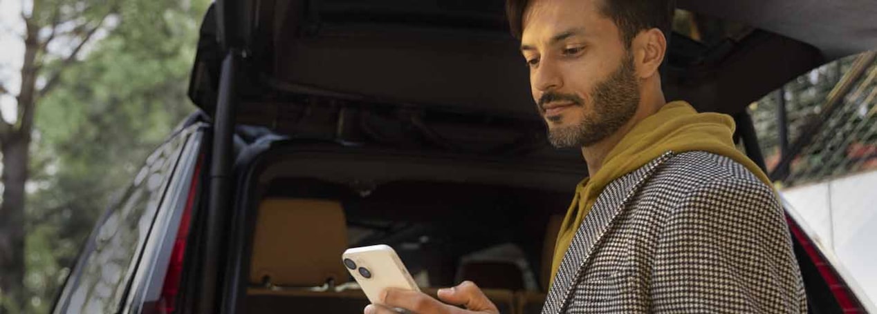 Gentleman standing by the open trunk of his vehicle while looking at his smartphone.
