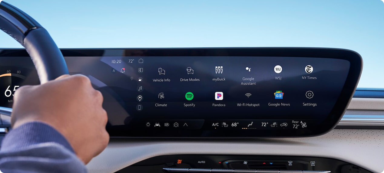 A hand rests on a car steering wheel, with a wide infotainment screen displaying apps like Google Maps and YouTube.