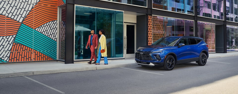 Couple holding hands while walking down a colorful city street and passing a GM vehicle