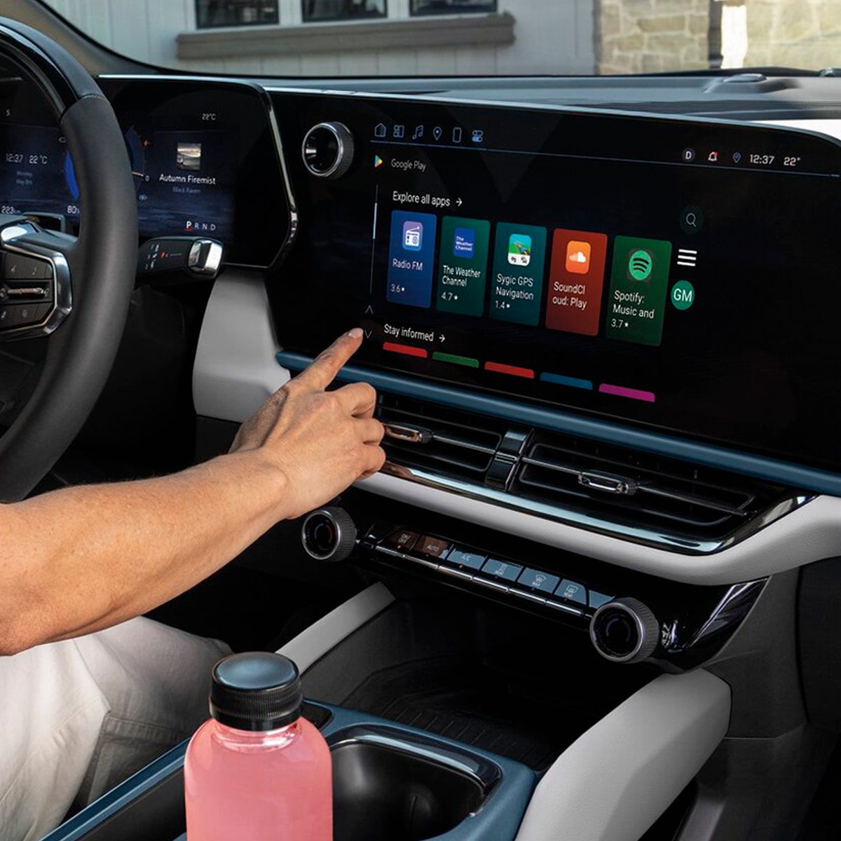 A man in the driver seat reaching to touch a button on the infotainment screen.