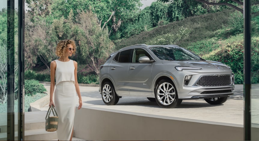 A woman walking into her house with her Buick vehicle parked in the driveway