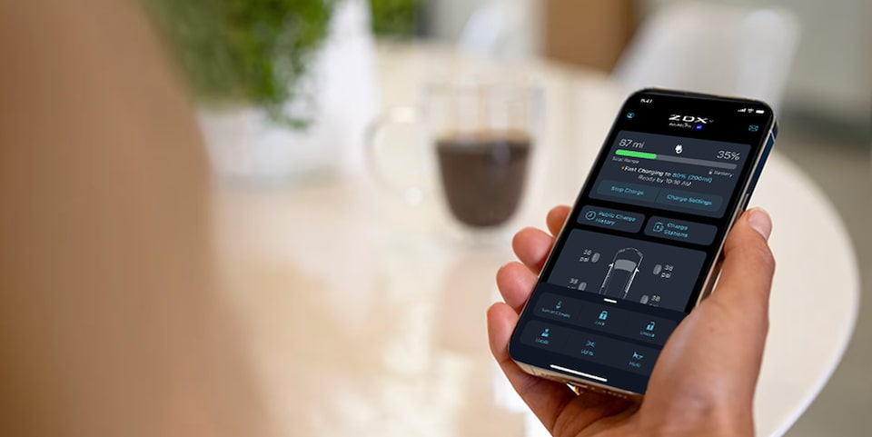 A person holds a smartphone displaying the AcuraLink app with car status and controls.