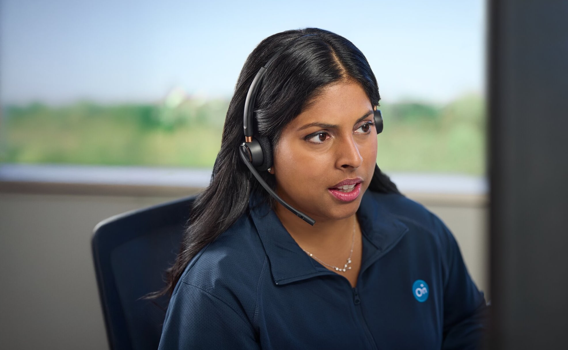 An OnStar advisor wearing a headset looks intently at a screen, wearing a navy blue polo shirt with the OnStar logo.
