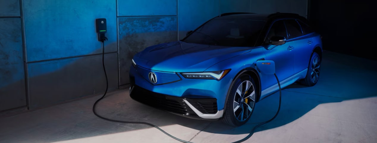 A blue electric Acura vehicle is charging at a wall charger in a modern garage.