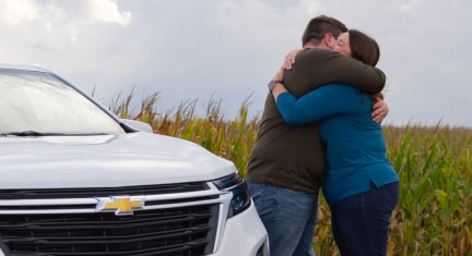 A mother and son hugging while standing next to their Chevy vehicle.