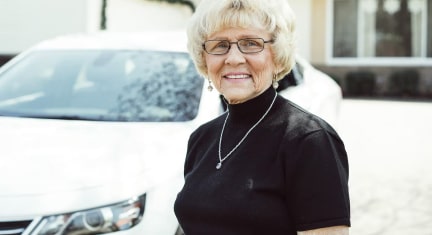 Older Woman Smiling Standing in Front of Chevy Car
