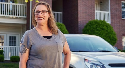 Nicole Kutas smiles while standing next to her Chevy in front of an apartment building.