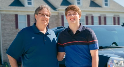 Father and Son Standing Side by Side in Driveway Smiling 