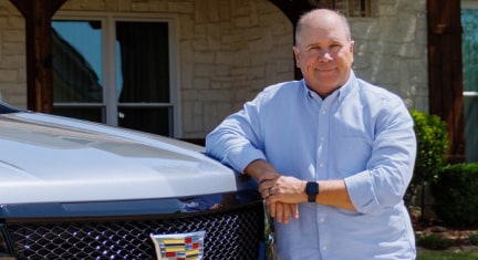 Eric in a blue polo shirt leaning onto the hood of his Cadillac SUV