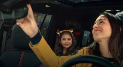 A woman in the driver’s seat pressing the OnStar button while smiling at her daughter in the back seat.