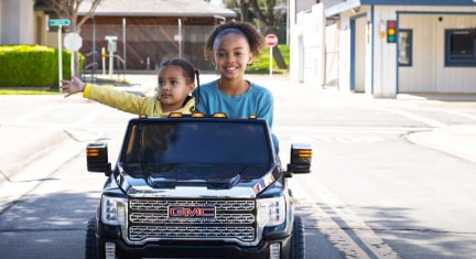 Two Kids in a Mini Play Car Driving Down the Road