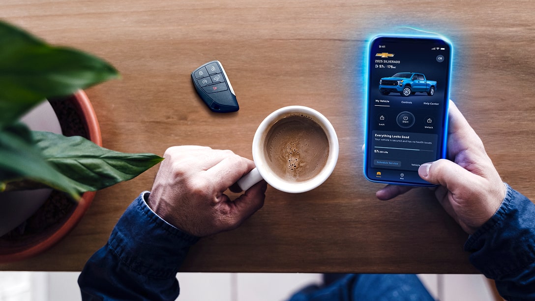 A male holding a cup of coffee while using his vehicle remote control on his smartphone.