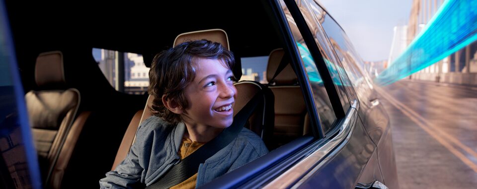 A young boy smiling while looking out the window of a moving vehicle