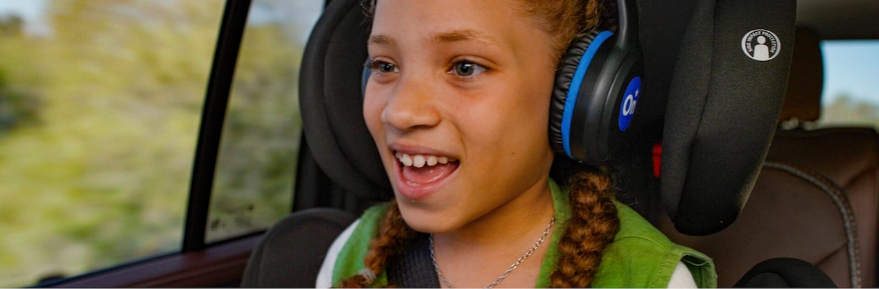 A girl sitting in her booster seat with over the ear headphones.