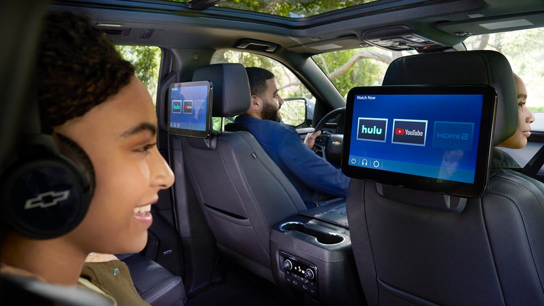 A girl sitting in the back seat watching a screen attached to the passenger seat in front of her.