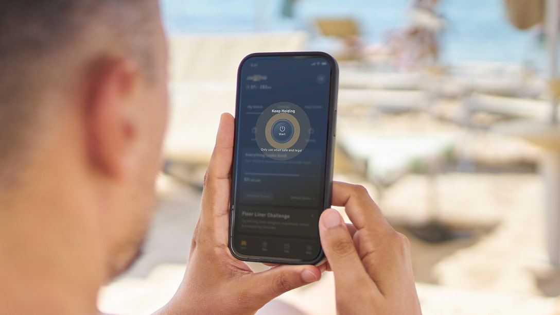 A behind the head view of a man holding a smarphone looking at his OnStar app.