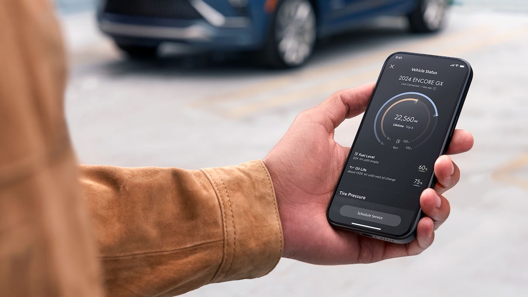 A hand holds a smartphone displaying the OnStar Guardian mobile app, which shows a map with a car icon and a location pin in a parking lot, demonstrating the vehicle locate feature.