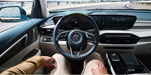 A driver's hands rest on their lap, behind the steering wheel of a Buick vehicle, indicating hands-free driving.