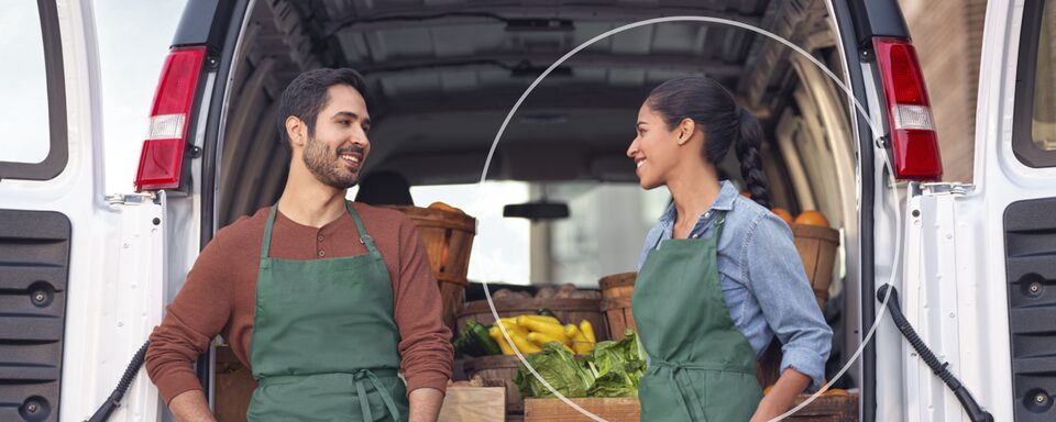 Two People Wearing Aprons Standing at the Rear of a Work Van