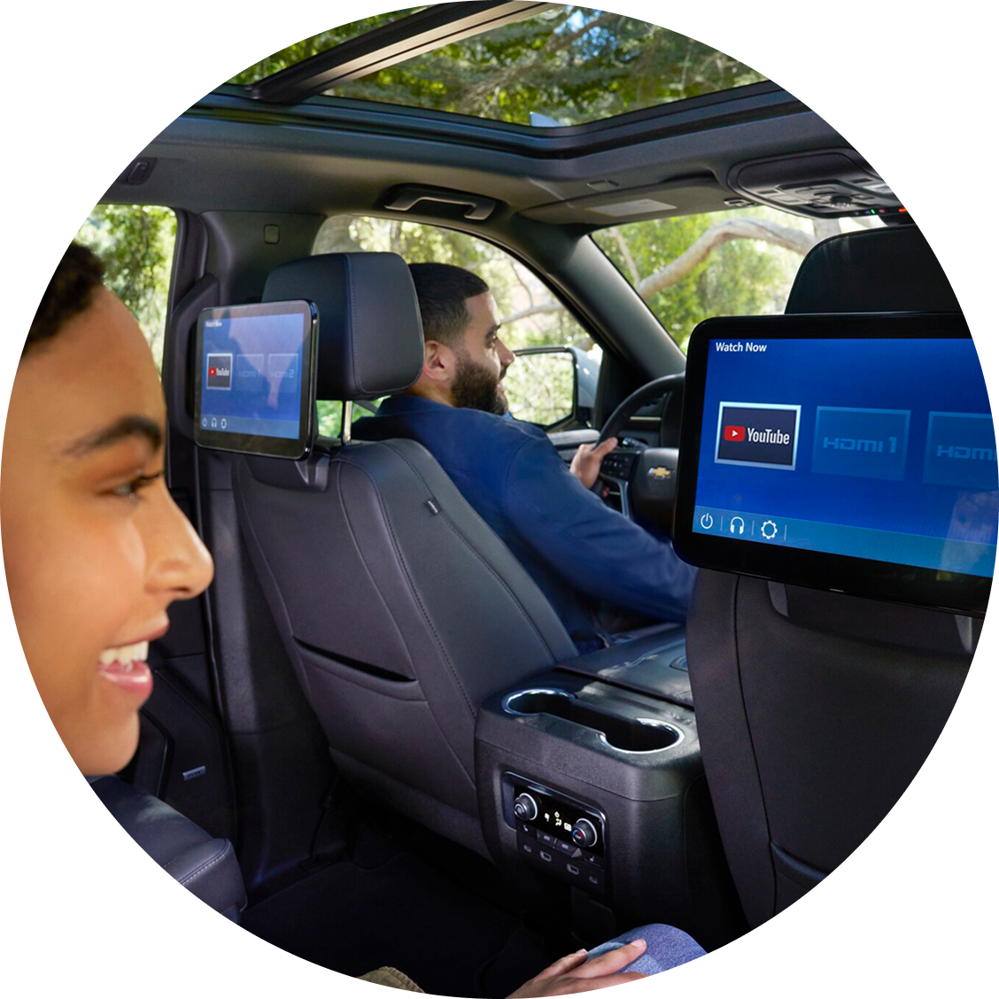 A young woman sitting in the backseat smiling and looking at the screen attached to the seat in front of her.