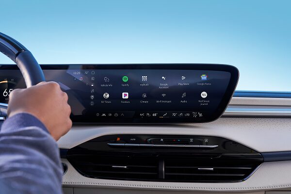 A driver's hand is visible on the steering wheel, while the vehicle's large center console screen is displaying a variety of OnStar in-vehicle apps, including audiobooks, podcasts, and music services.