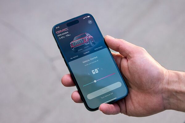 A hand holds a smartphone displaying the GMC OnStar Guardian app, showing options to remote start the vehicle and adjust the interior temperature to 68 degrees, with a white truck shown at the top of the screen.