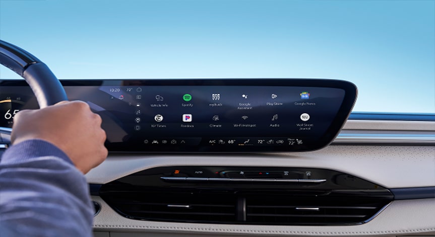 A driver's hand is visible on the steering wheel, while the vehicle's large center console screen is displaying a variety of OnStar in-vehicle apps, including audiobooks, podcasts, and music services.