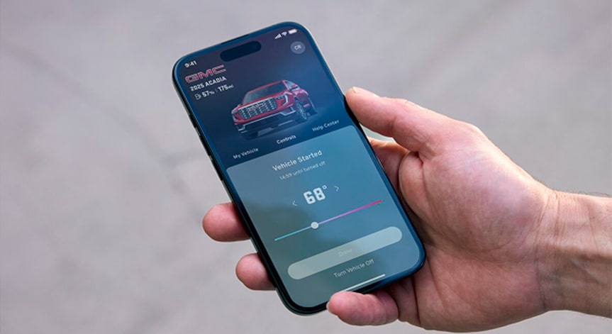 A hand holds a smartphone displaying the GMC OnStar Guardian app, showing options to remote start the vehicle and adjust the interior temperature to 68 degrees, with a white truck shown at the top of the screen.