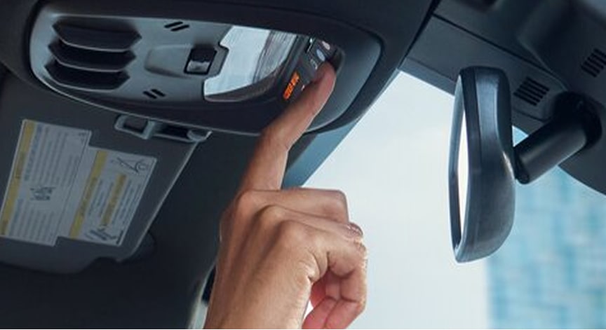 A hand reaches up to press an orange emergency button on the overhead console of a car.