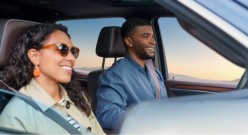 A smiling couple wears seatbelts while driving in the front seats of a car.