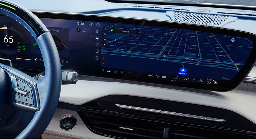 Interior of a Cadillac car with a large curved display showing a navigation map and a digital speedometer at 65 mph.