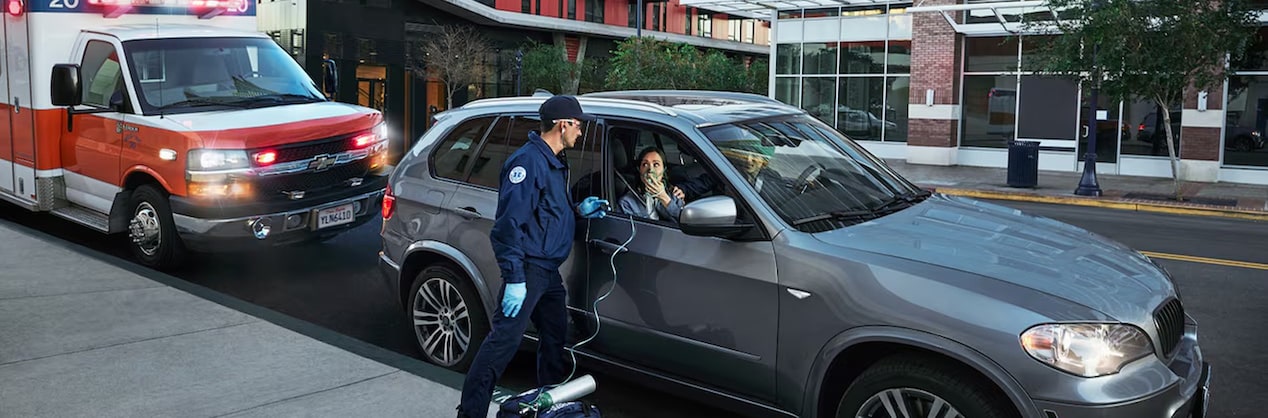 A first responder standing next to a vehicle and talking to a woman sitting in the passenger seat of a vehicle.