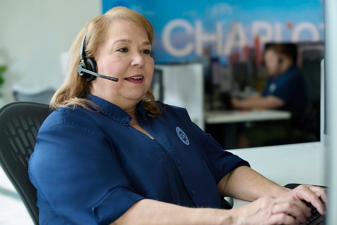 A female OnStar employee talking with her headset on and typing on her computer.
