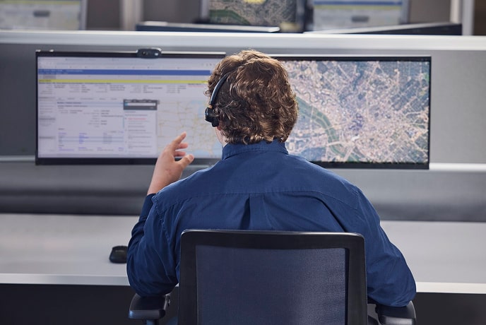 A behind view of a male OnStar employee talking on his headset and looking at his two computer monitors.
