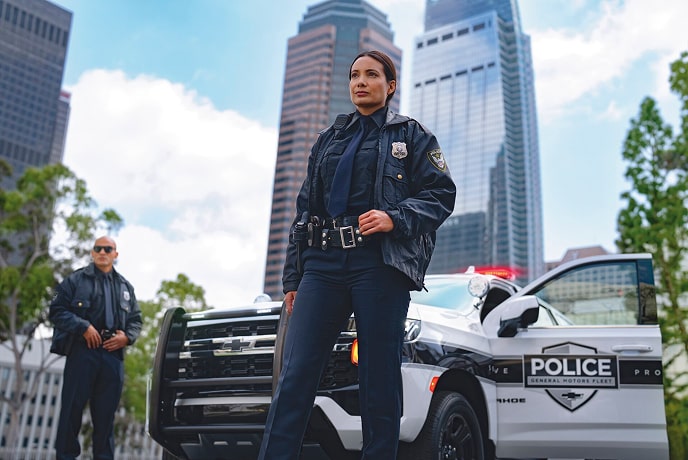 Two police officers, one male and one female, standing in front of their police SUV.