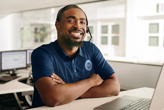A male OnStar employee sitting with his arms crossed and smiling while wearing his headset.