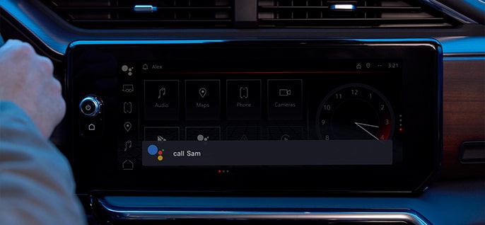 A hand interacts with a car's infotainment screen displaying "Call Sam" with the Google Assistant icon for voice commands.