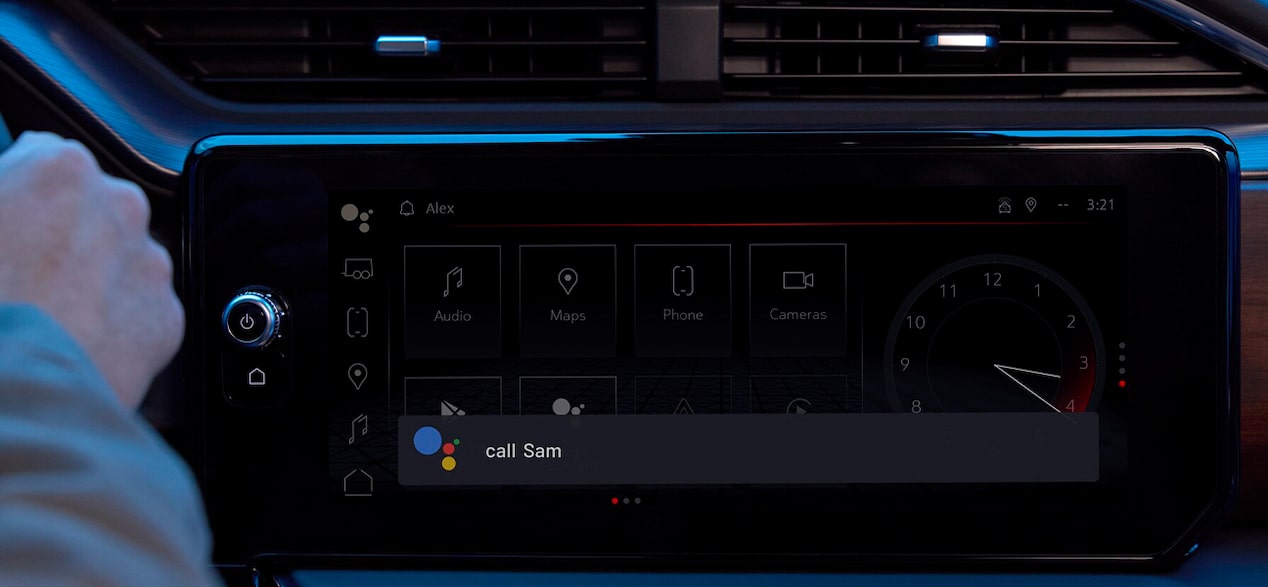 A hand interacts with a car's infotainment screen displaying "Call Sam" with the Google Assistant icon for voice commands.