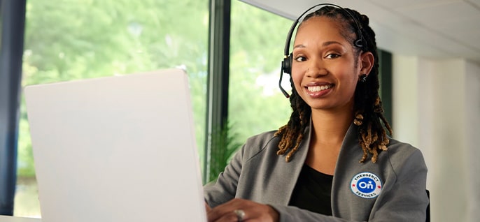 An OnStar customer service representative, wearing a headset, smiling at a laptop with a visible OnStar logo on her jacket.