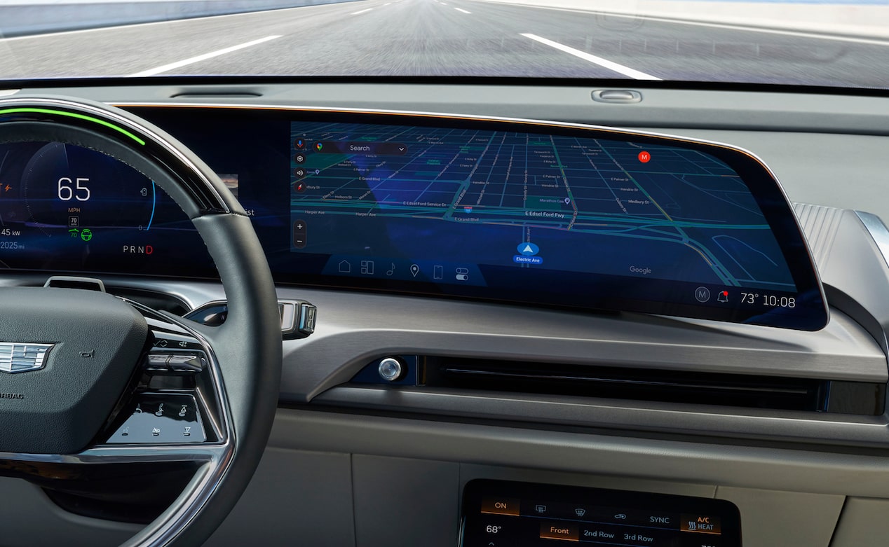 A man in a car points at a large, brightly lit infotainment screen displaying various application icons.