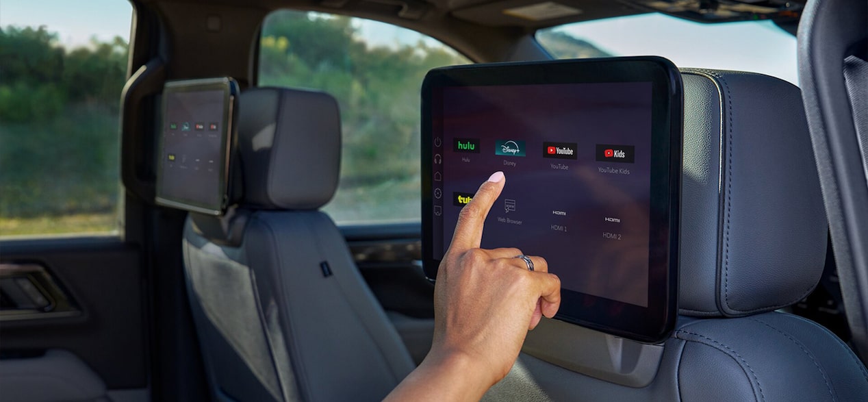 A hand interacts with a rear seat entertainment screen showing app icons like YouTube and Disney+.