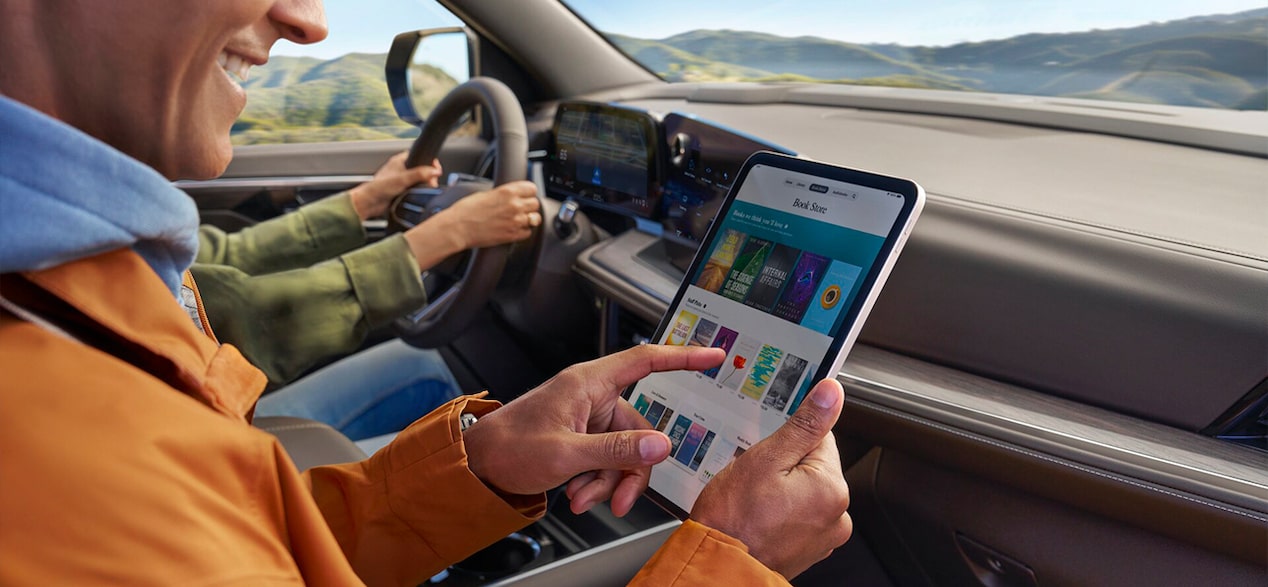 A passenger in a car holds a tablet displaying app icons.
