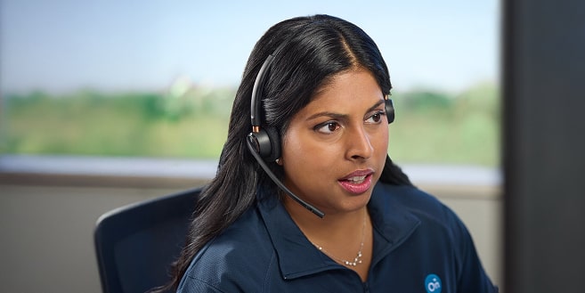 An OnStar advisor wearing a headset looks intently at a screen, wearing a navy blue polo shirt with the OnStar logo.