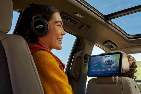 A Woman Sitting in the Left Rear Passenger Sear with Headphones On While Facing the Screen