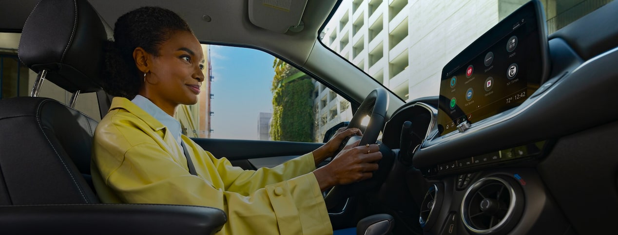 A woman in a yellow jacket sits in the driver's seat of a vehicle with a large infotainment screen displaying app icons like Spotify and Pandora, showcasing the integrated technology and entertainment features supported by OnStar.